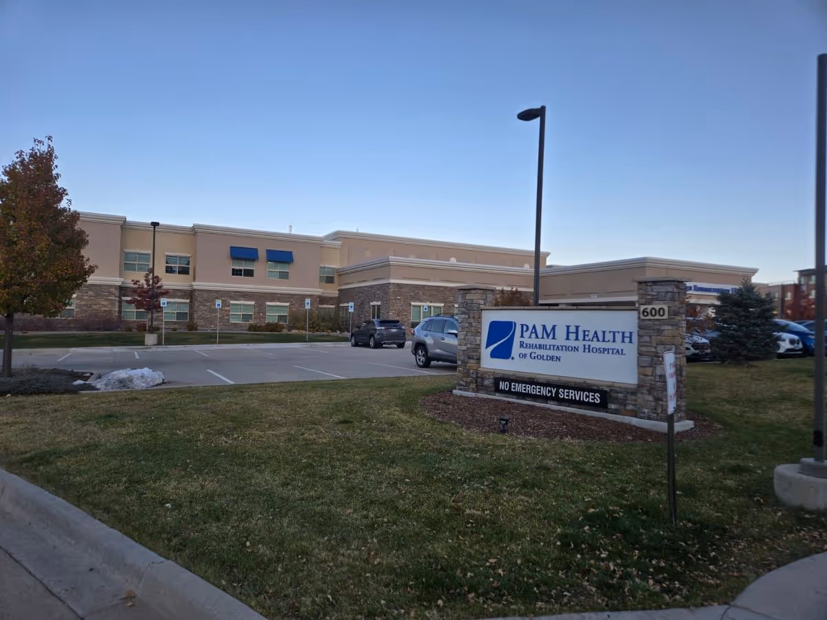 Front exterior of PAM Health Rehabilitation Hospital of Golden with its sign, parking lot, and a two-story beige building.