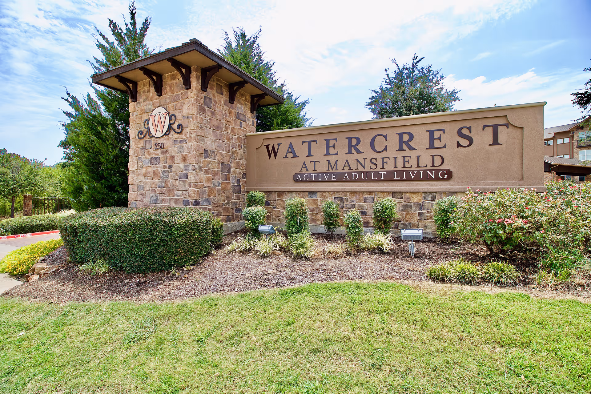 Stone entrance sign reading 'Watercrest at Mansfield Active Adult Living' surrounded by trimmed shrubs and lawn.