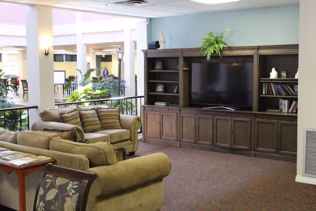 Comfortable common lounge area with sofas facing a large entertainment cabinet and TV in an indoor atrium.