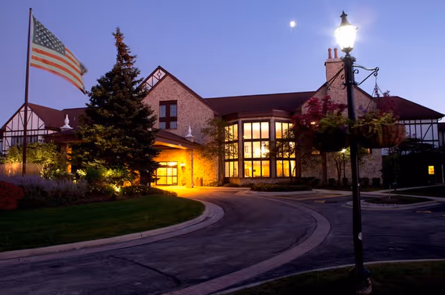 Evening exterior view of Covenant Living at Windsor Park with lit entrance and flag.