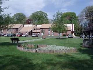 Exterior view of Whitinsville Retirement Society with green lawn and circular garden bed.