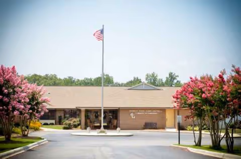 Front exterior of Stanley Total Living Center with flagpole and pink flowering trees.