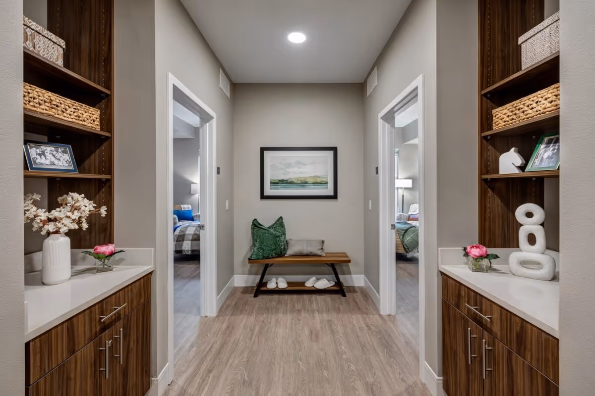 Interior hallway with wood built-in cabinets, decorative shelving and a bench between two bedroom doorways.