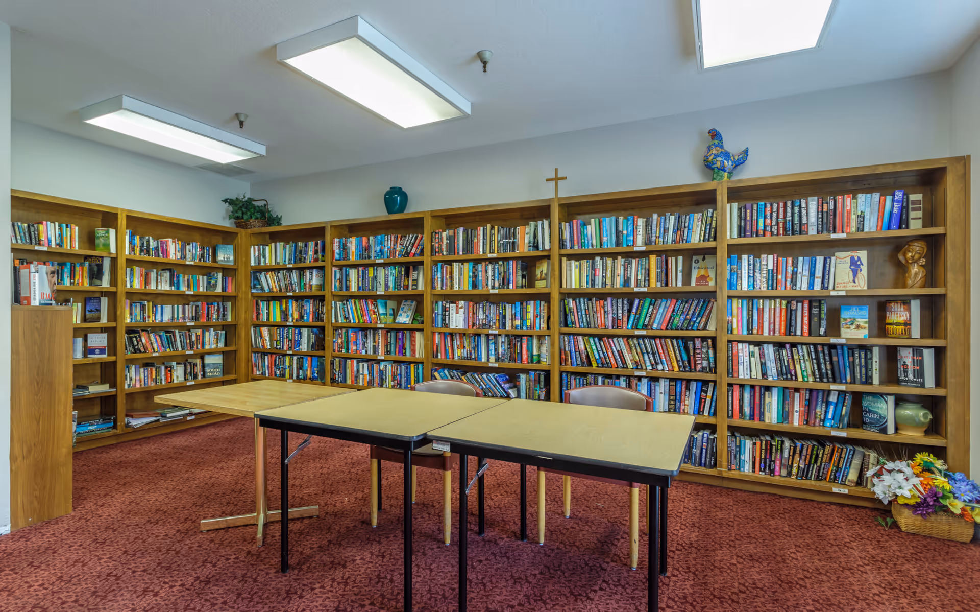 Interior reading room with bookshelves lining the walls, tables and chairs on a red carpet.