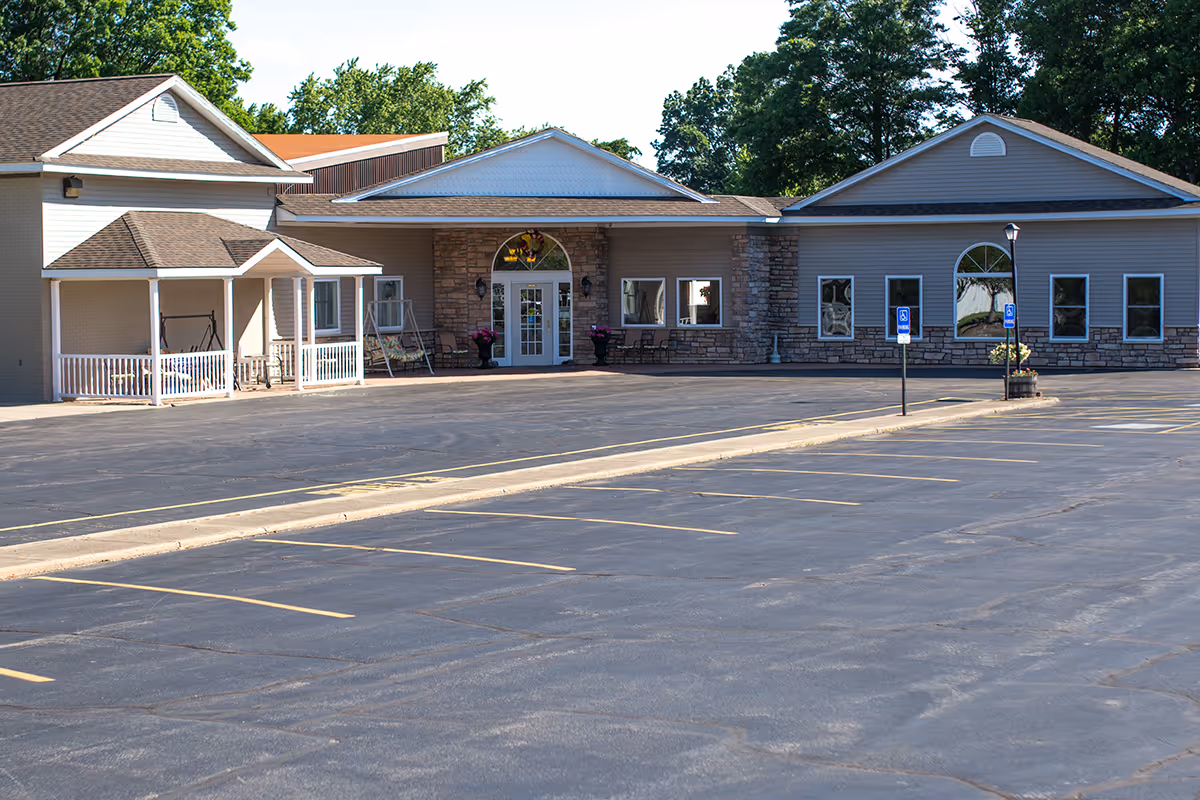 Exterior view of Clearview Lantern Suites building with a large empty parking lot in front, featuring accessible parking spaces and a covered entrance with seating and flower pots.