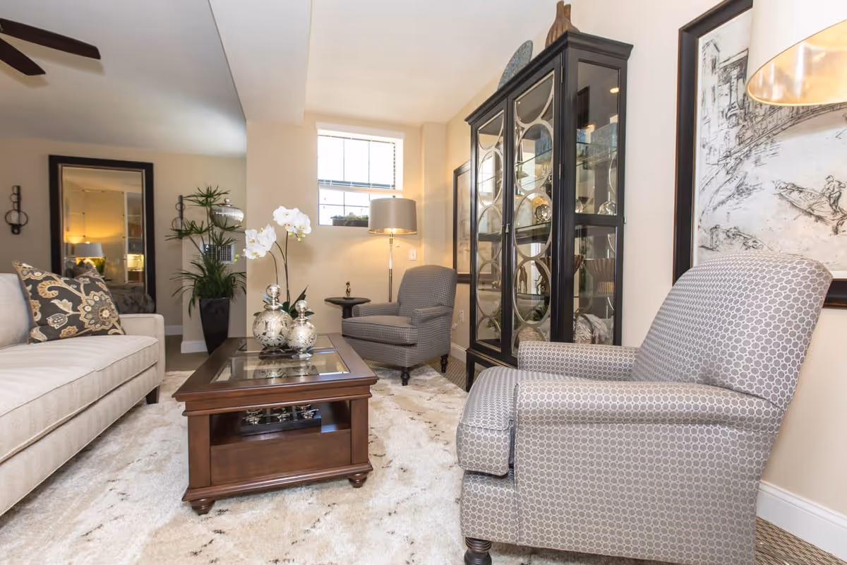 Well-decorated living room with upholstered chairs, a sofa, coffee table, rug, and a glass display cabinet.