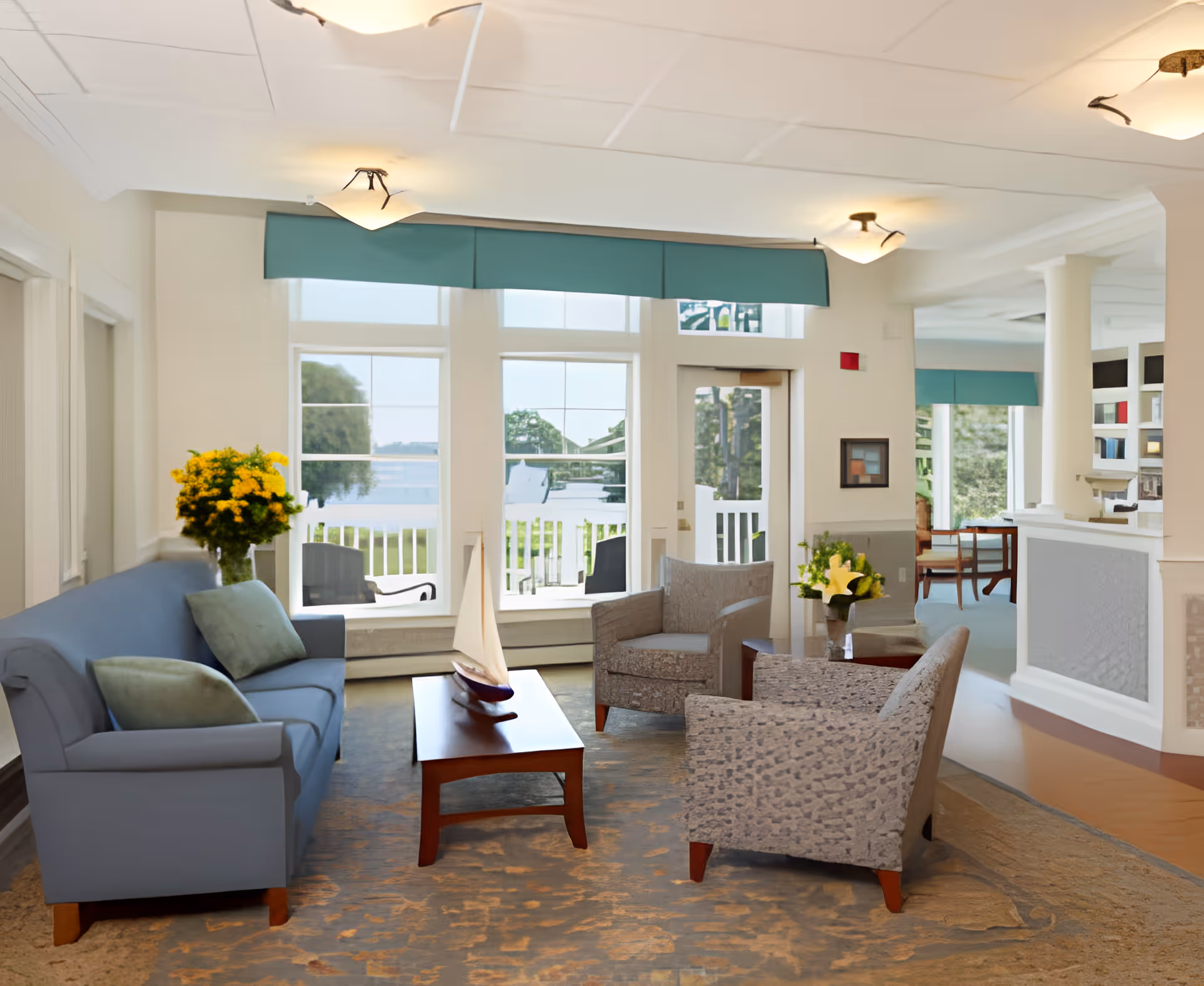 Bright sitting area with a blue sofa, armchairs, coffee table and large windows overlooking a water view.