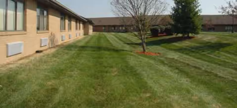 Exterior view of a brick senior facility with a green lawn and trees.