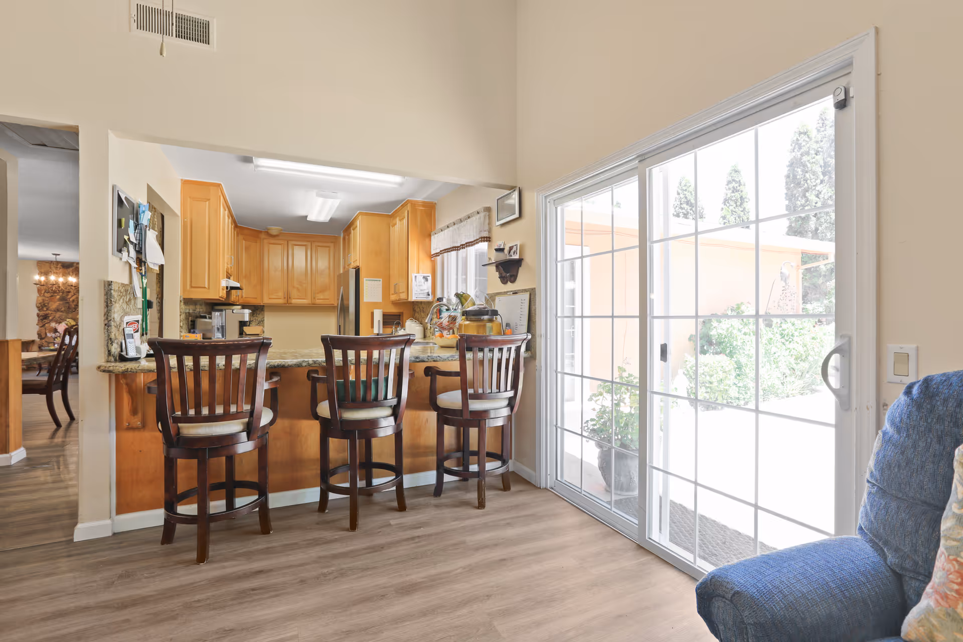 Open kitchen with a granite breakfast bar, three wooden bar stools, and a sliding glass door to the patio.