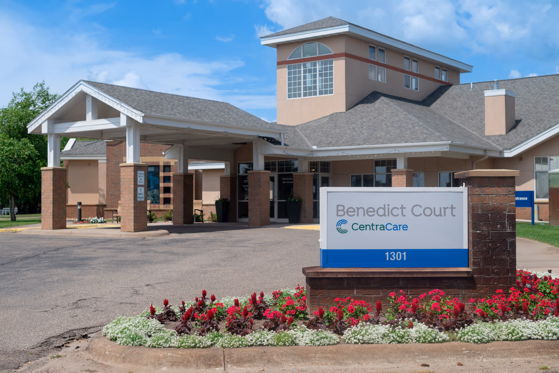 Front entrance of Benedict Court CentraCare senior living community with a covered drop-off and a sign reading 'Benedict Court CentraCare 1301'.