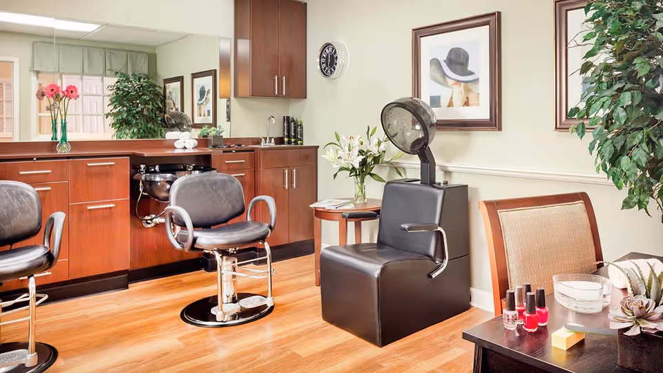 A bright salon interior with barber chairs, a hooded hair dryer, manicure supplies, and wood cabinetry.