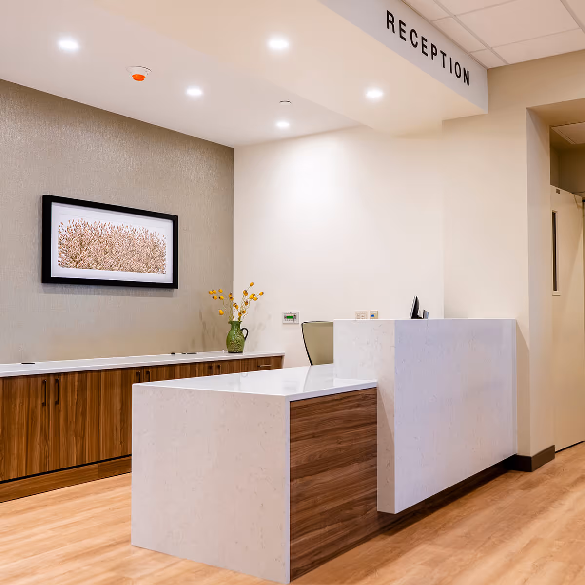 Modern reception area with a white marble desk, wood cabinetry, framed wall art, and a 'RECEPTION' sign overhead.