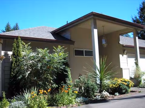 Front exterior of a single-story building with a covered entrance and lush landscaped garden.
