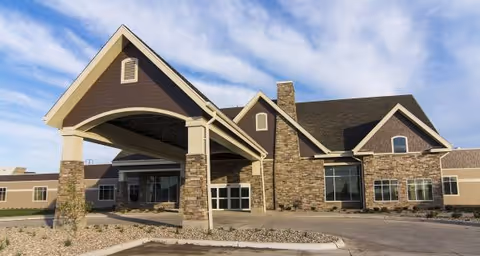Front view of Prairie Ridge Care Center with stone facade, arched entrance, and blue sky.