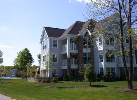 Exterior view of a multi-story retirement community building with balconies and landscaped grounds.