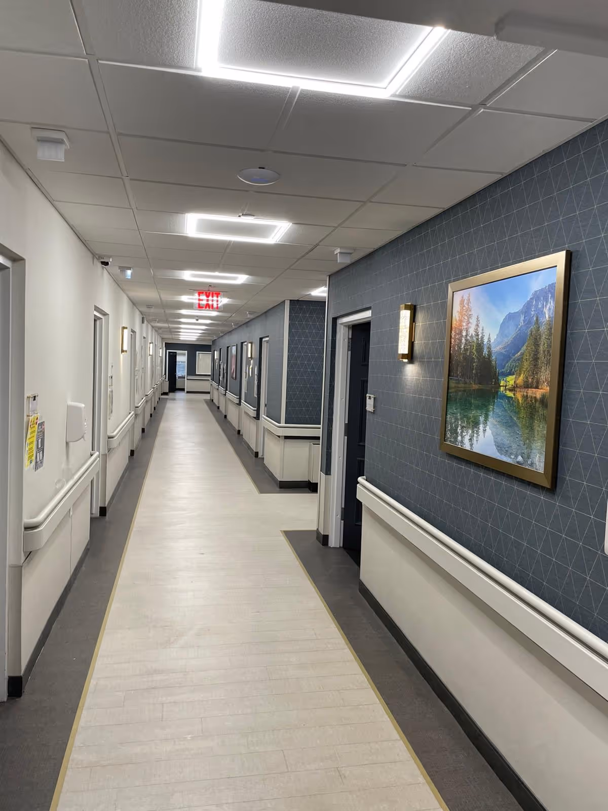 Long, well-lit interior corridor with handrails, framed artwork, and multiple doorways.