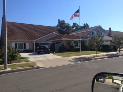 Front view of a one-story senior living facility with a flagpole and driveway.