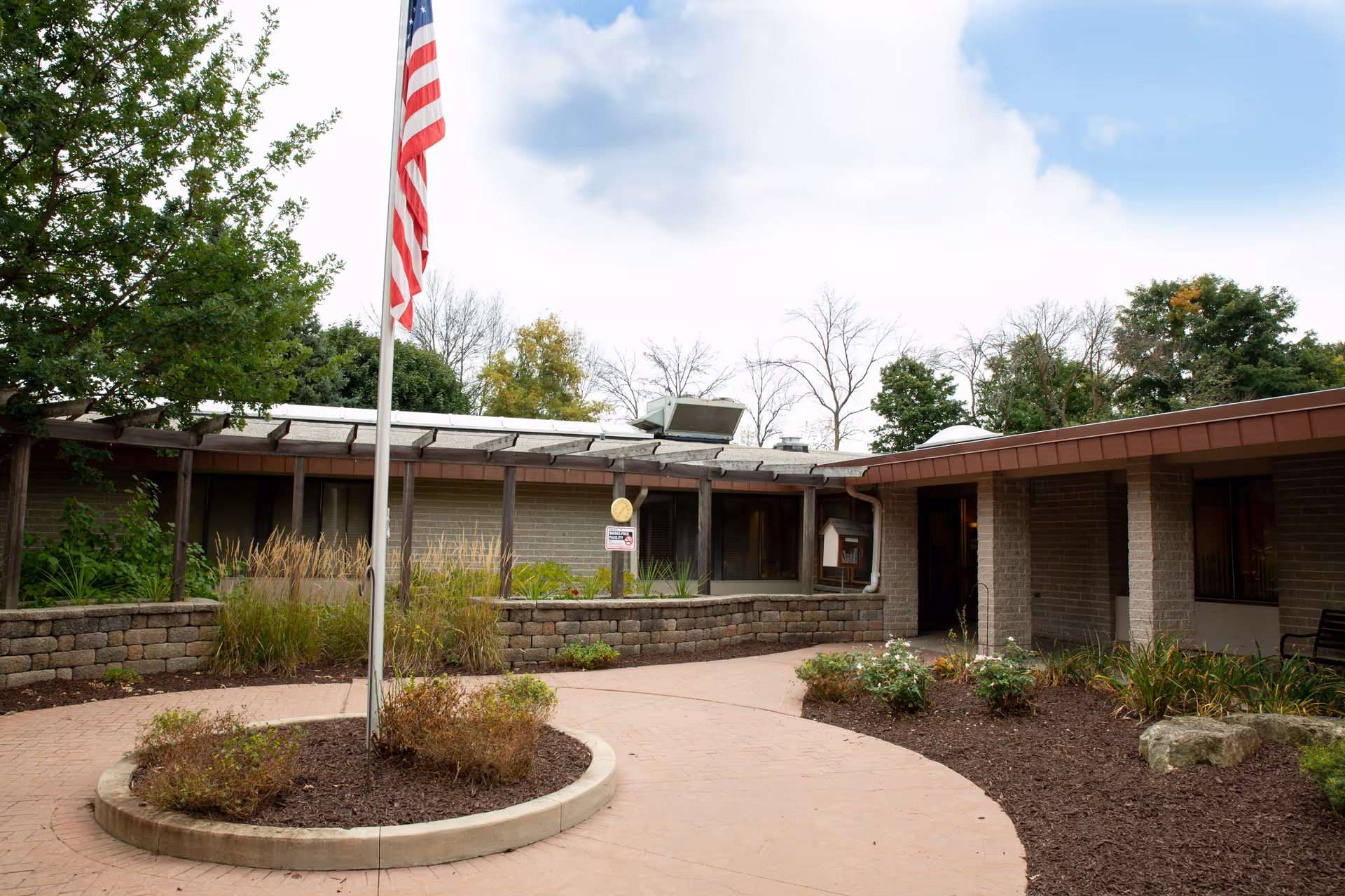 Courtyard and entrance of a single-story brick senior living facility with an American flag in front.