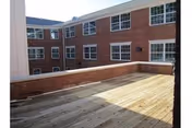 A spacious outdoor wooden deck area surrounded by brick walls and windows of a multi-story building under a clear sky.