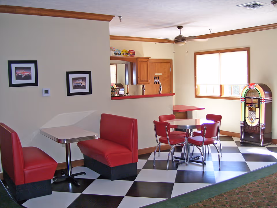 Retro diner-style common area with red booth seating, a round chrome table, black-and-white checkered floor and a jukebox.