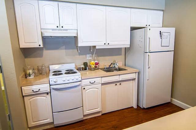 Small kitchenette with white cabinets, electric stove, sink, and refrigerator.