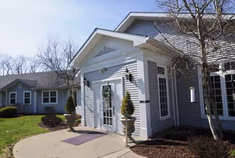 Front entrance of a gray senior living facility with double doors and shrubs.