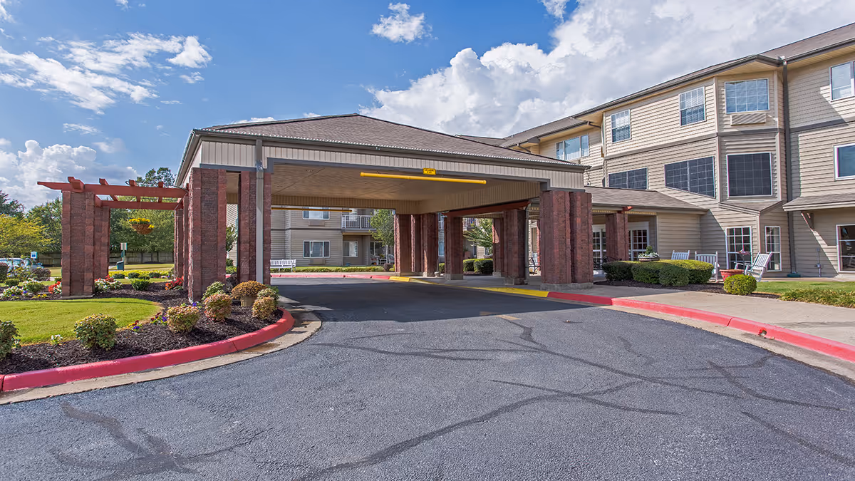 Covered porte-cochere entrance of a multi-story senior living building with landscaped flower beds and a driveway.