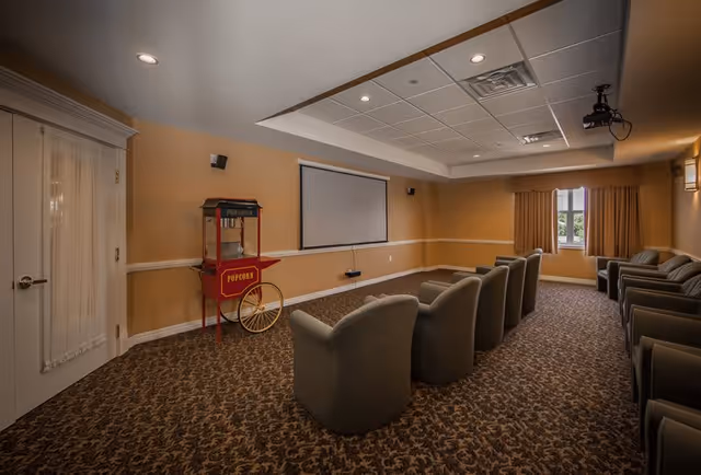 A small screening room with upholstered chairs facing a projection screen and a vintage popcorn cart.