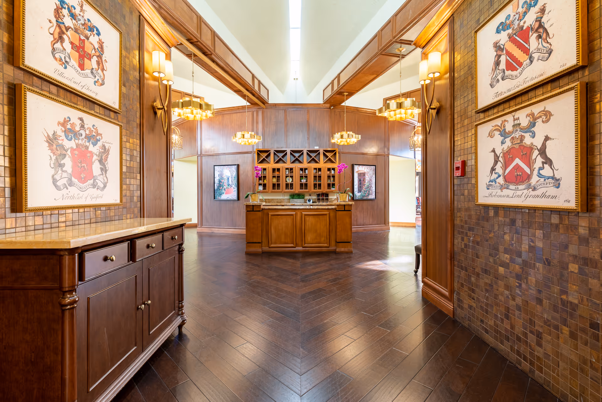Warm wood-paneled interior lobby with a central wooden island, chandeliers, and framed crests on the walls.