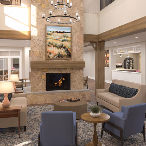 Spacious sitting area with a stone fireplace, chandelier, multiple armchairs and sofas arranged around coffee tables in a communal lounge.