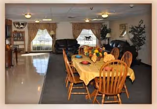 Dining room area with a table covered by a yellow tablecloth and wooden chairs.