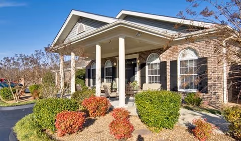 A brick Eiffel Gardens senior living facility with a covered front porch and trimmed shrubs.
