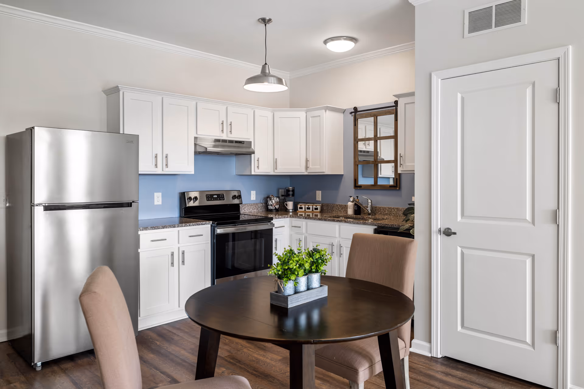 Modern kitchen with white cabinets, stainless steel appliances, and a round dining table with chairs and a small potted plant.