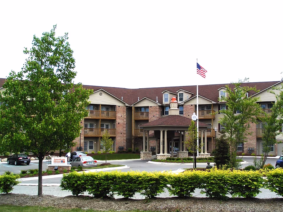 Exterior view of American House Milford senior living facility with entrance and landscaping.
