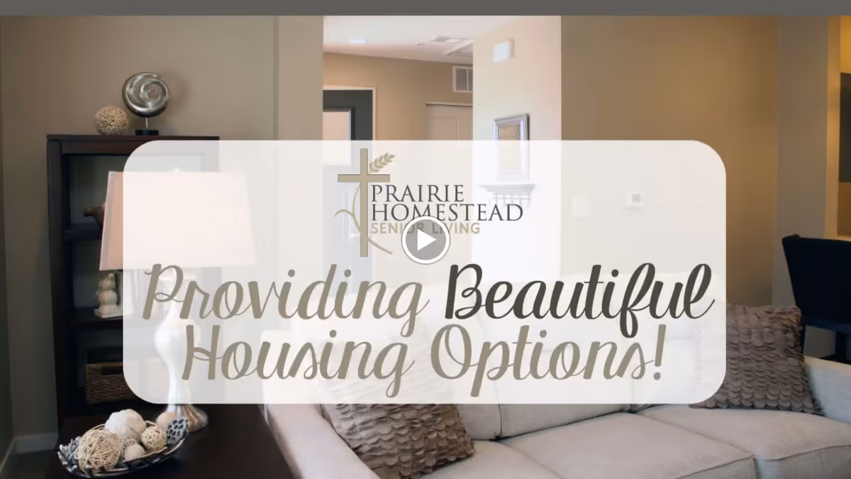 Living room with a sofa, decorative pillows, side table and lamp, overlaid by a translucent banner reading "Providing Beautiful Housing Options!"