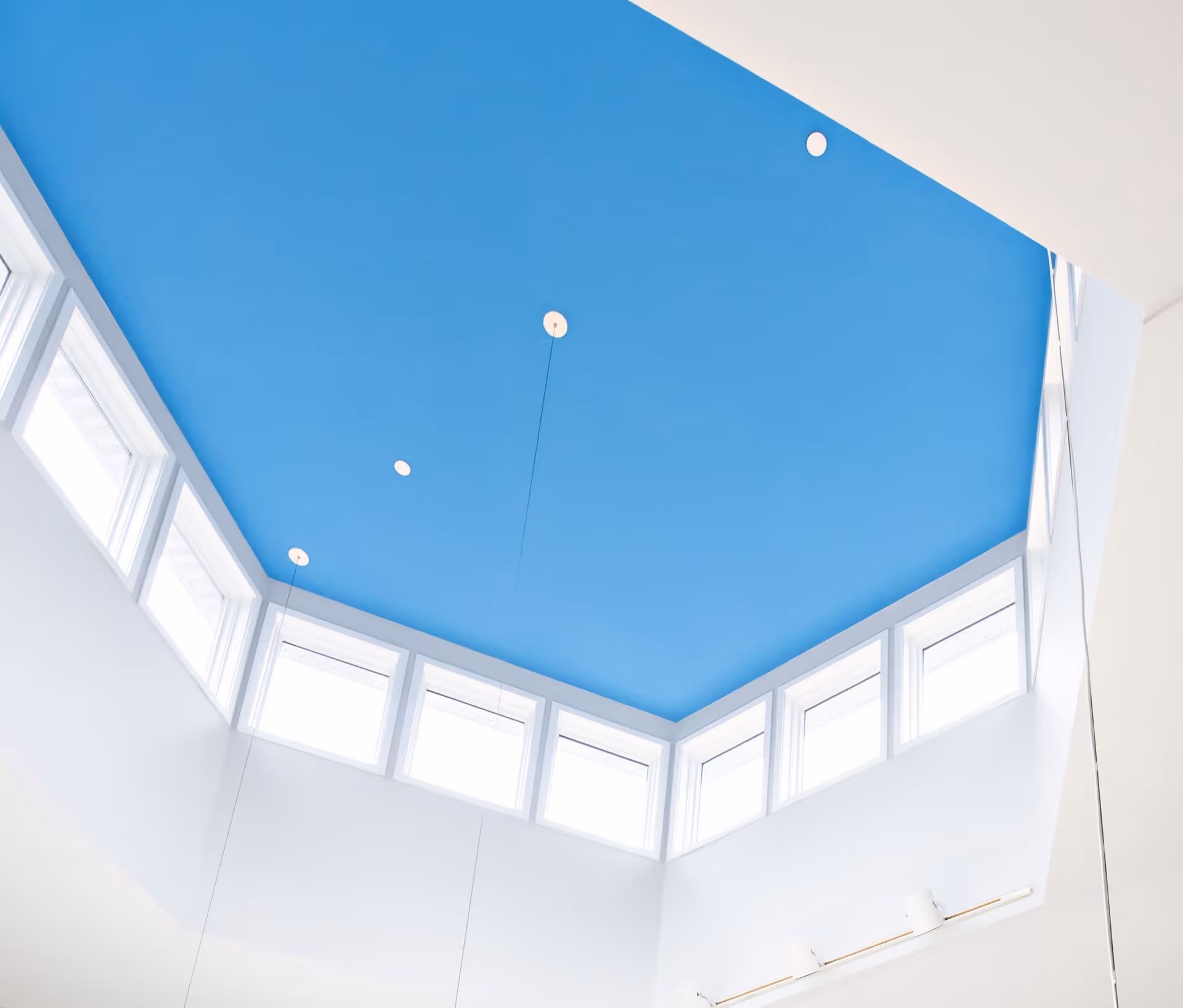 Looking up at a bright blue vaulted ceiling with clerestory windows and recessed lights in a white interior.