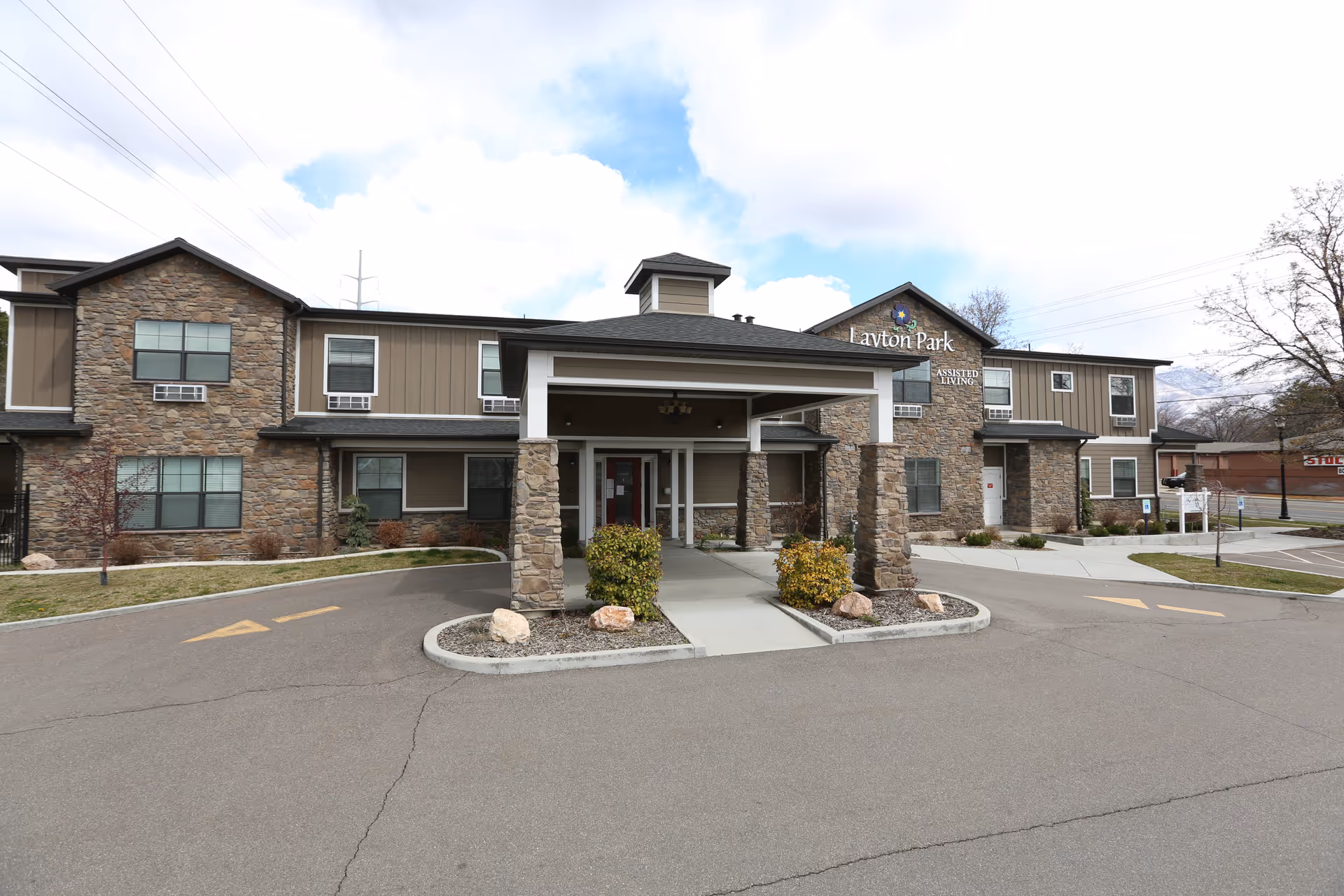 Front view of Layton Park Memory Care assisted living building with a covered entrance, stone columns, and driveway.