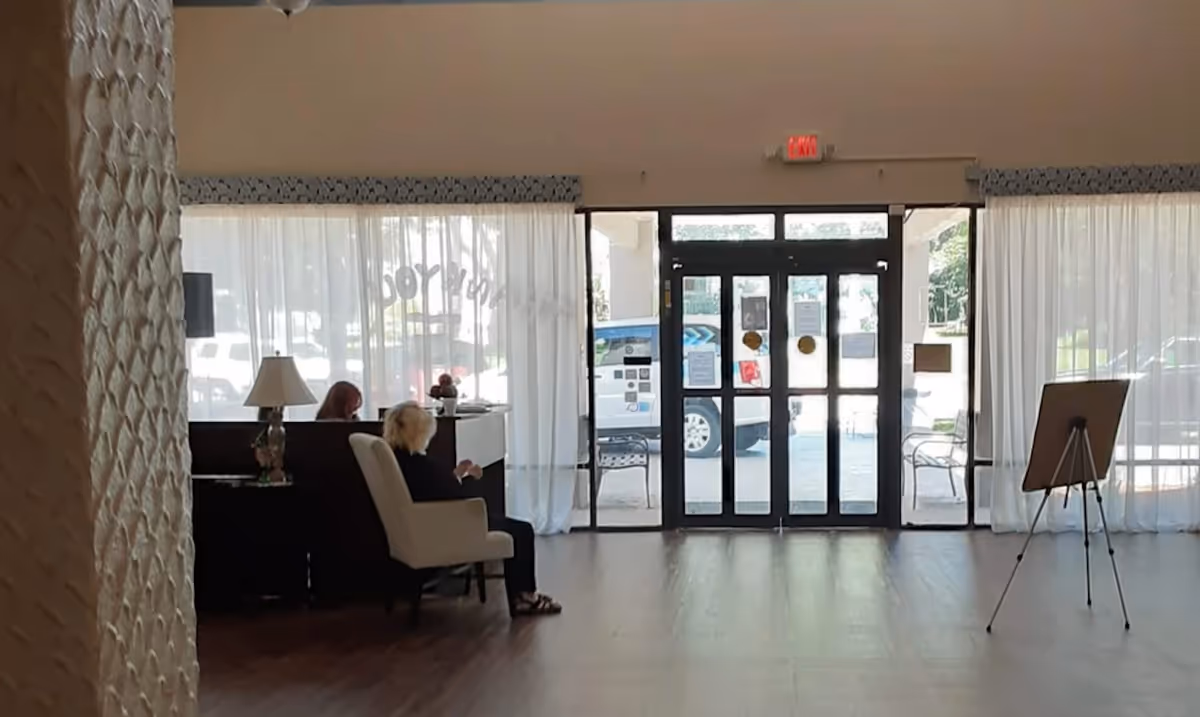 Interior lobby with chairs and a reception desk to the left and double glass entrance doors straight ahead.
