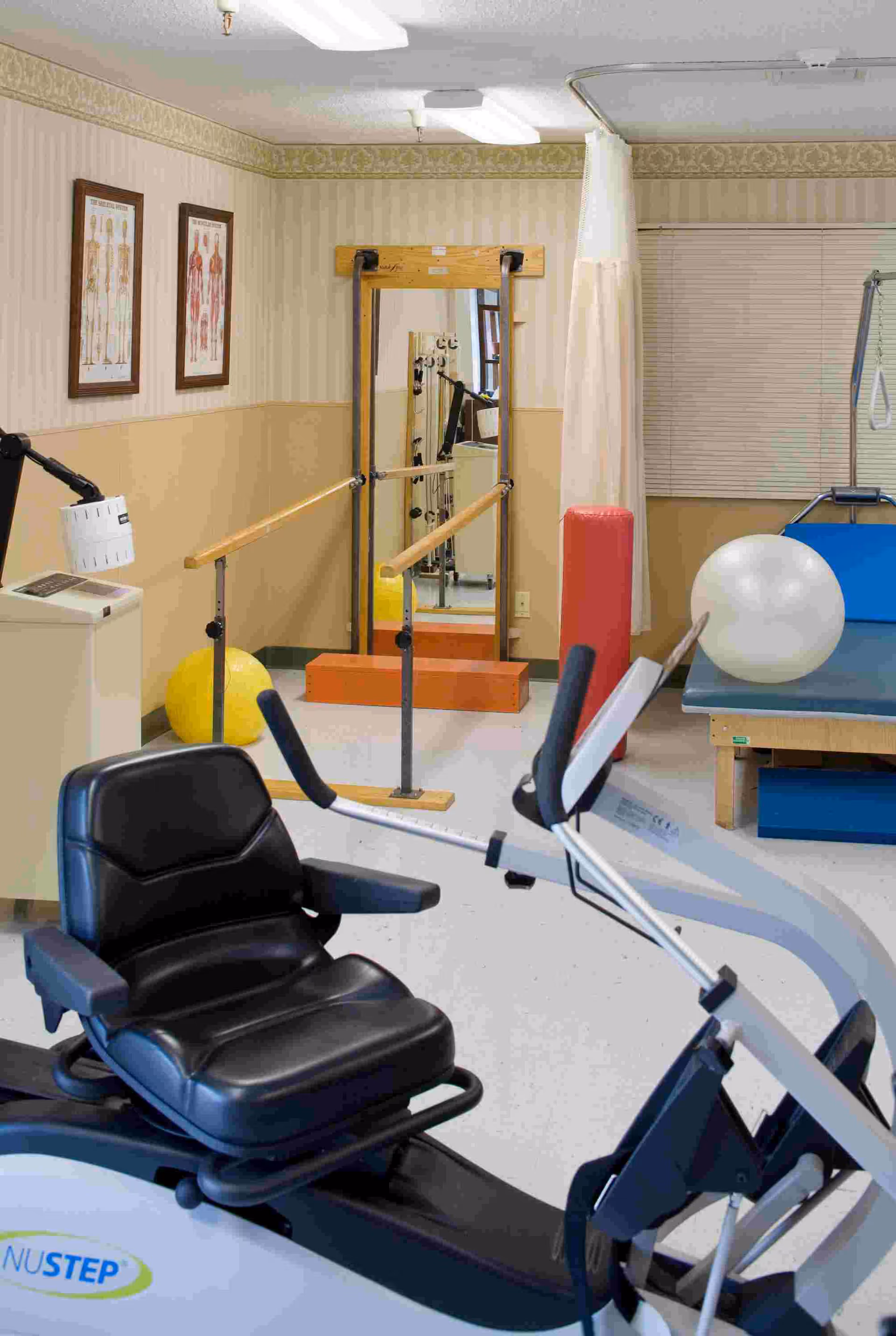 Therapy room with a recumbent exercise bike, parallel bars, a large exercise ball and a treatment table.