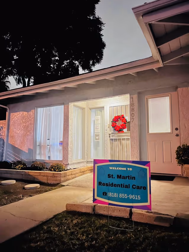 Front entrance of St. Martin Residential Care at dusk with a welcome sign on the lawn and a red wreath on the door.