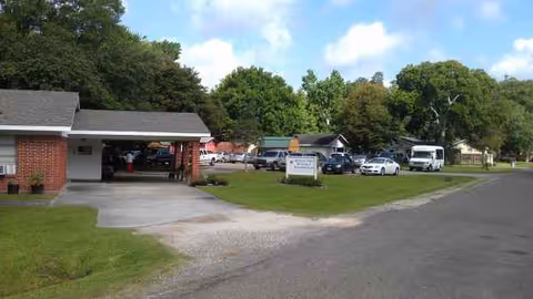 A single-story nursing facility with a driveway, parking lot, and a sign near the entrance.