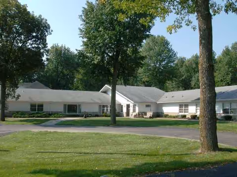 Exterior view of a single-story senior living facility with green lawn and trees.