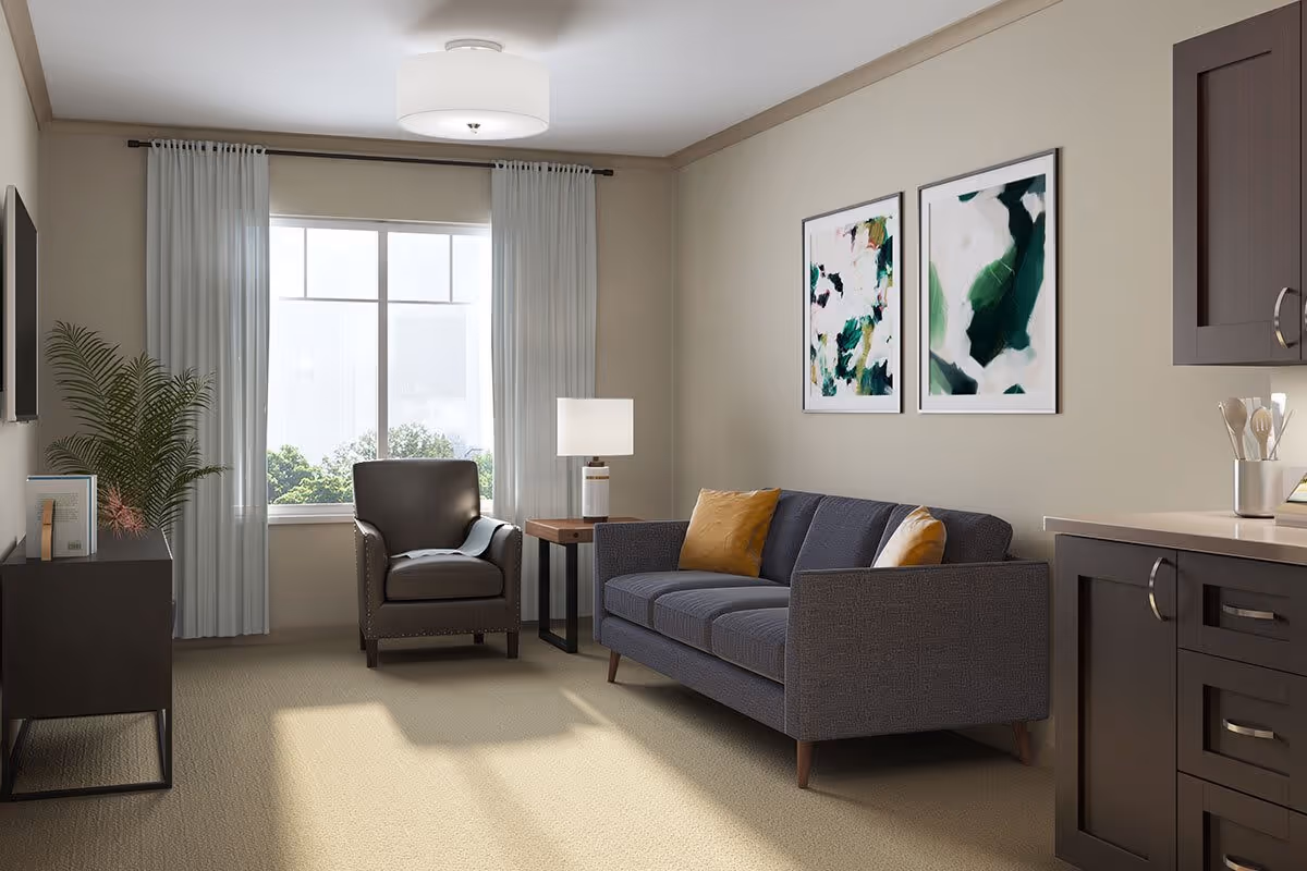A cozy living room with a gray sofa adorned with yellow and white pillows, a dark brown armchair, a wooden side table with a lamp, two abstract green and white paintings on the wall, a large window with white curtains, a flat-screen TV on a black stand, and a partial view of a kitchen counter with utensils.