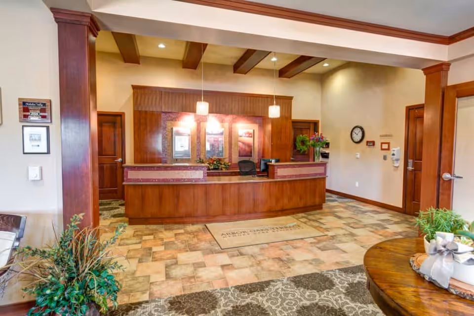 A wood-paneled reception desk in a memory care lobby with pendant lights, decorative plants and a tiled floor.