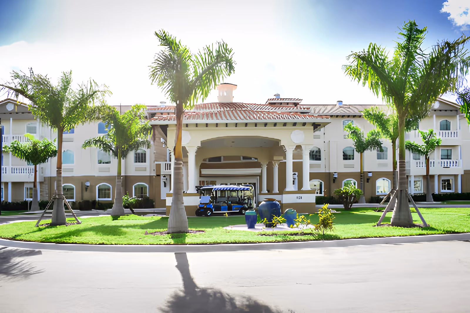 Front exterior view of Chateau Madeleine facility with a covered entrance, palm trees, green lawn, and a golf cart parked under the entrance canopy.