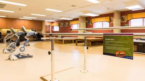 Interior rehab gym with parallel bars and exercise equipment in a senior living facility.