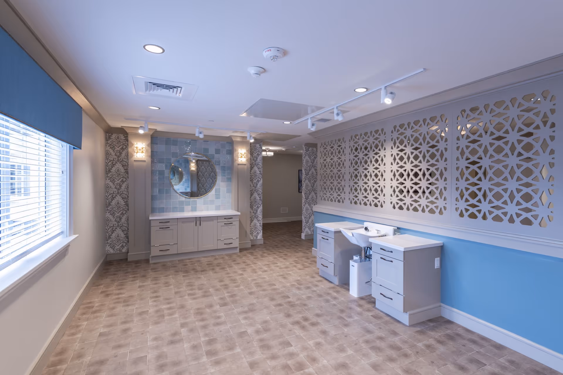 Well-lit interior room with vanities and sinks, a round mirror, decorative partition panels, and a large window.