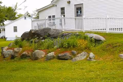 White senior living facility with a wooden deck and rocky landscaped yard.