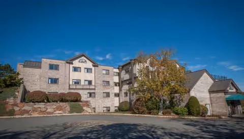 A multi-story stone senior living building with manicured landscaping and a clear blue sky.