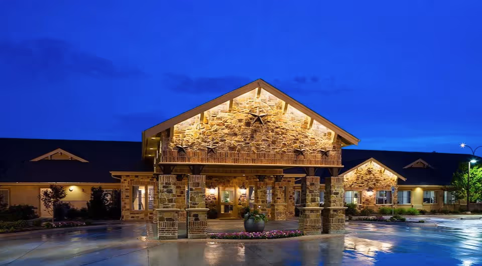 Stone-built memory care facility exterior lit at night with a welcoming entrance.